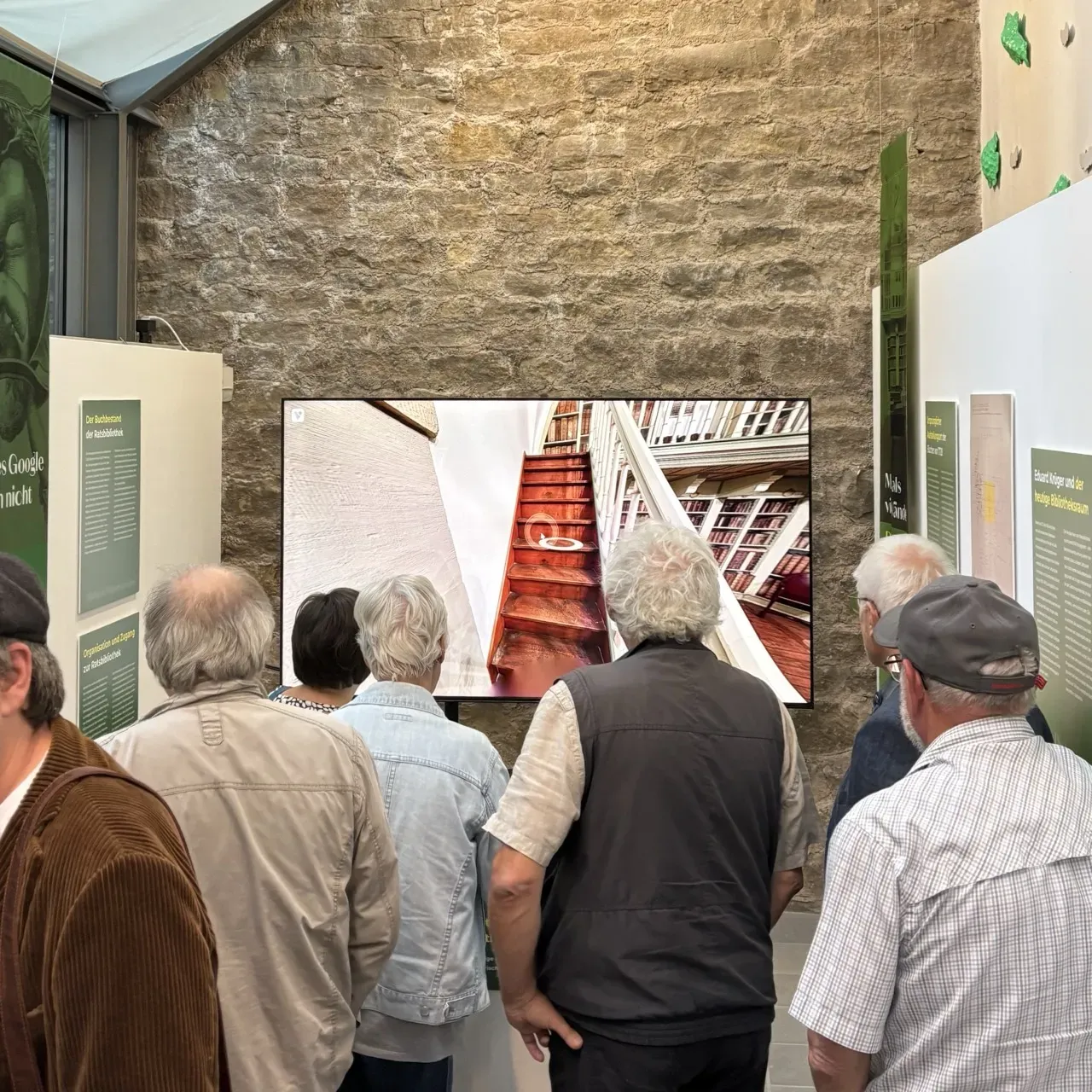 Besucher einer Ausstellung schauen auf einen großen Bildschirm mit einem 360°-Rundgang